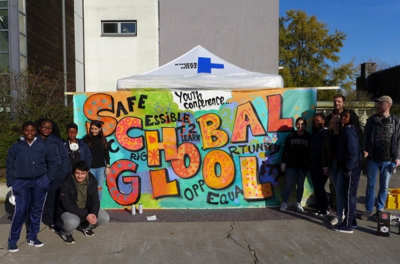 Jugendliche stehen vor Graffiti: "Schule Global"
