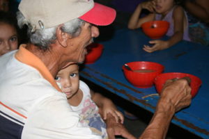 Ein alter Mann füttert ein kleines Kind auf seinem Schoß. (Quelle: Jürgen Schübelin)