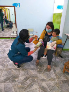 Eine Projektmitarbeiterin bietet einer Mutter Spielzeug für ihren kleinen Sohn an