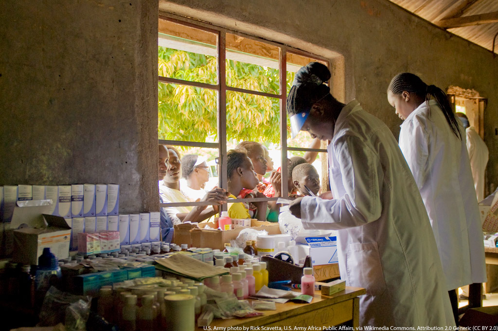 Medikamentenausgabe in Kenia: Gesundheitspersonal versorgt wartende Menschen durch ein Fenster eines Gesundheitszentrum mit Prophylaxe-Mitteln gegen Malaria